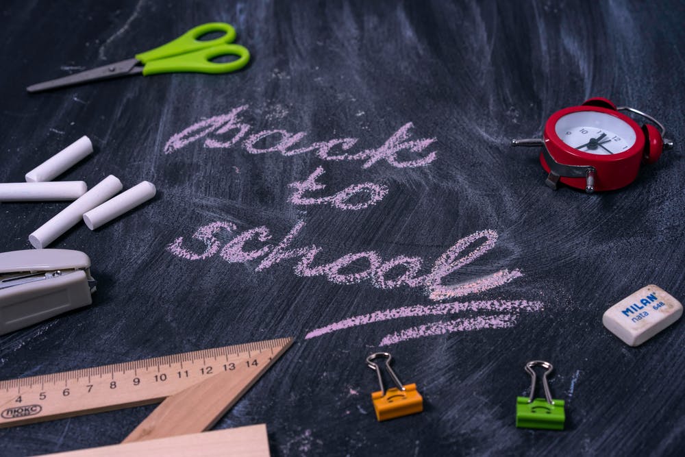 Back to School written on a chalk board with scissors, binder clips and other school supplies