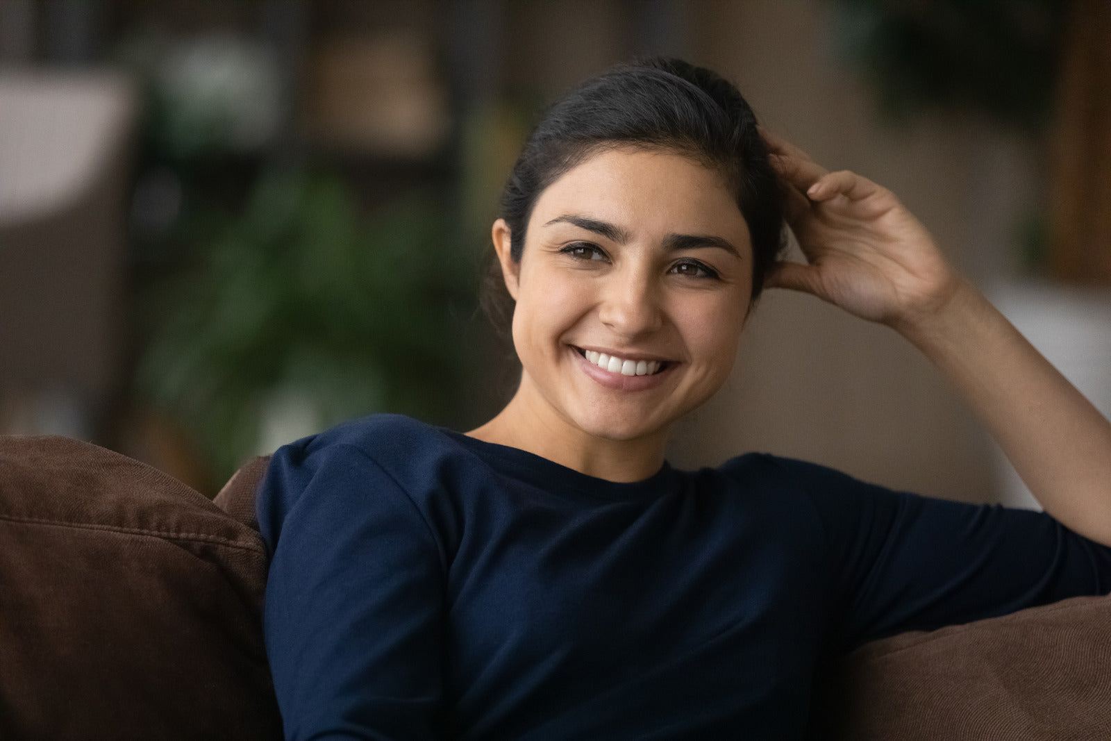 Indian woman sitting on couch smiling and looking off to the side