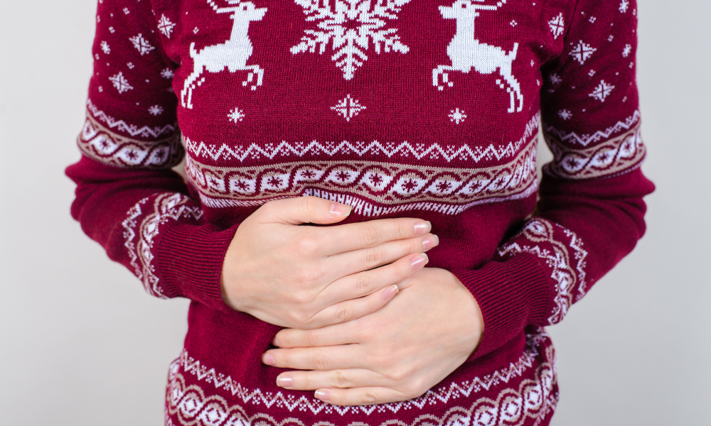 Woman Wearing Holiday Sweater Holding Stomach From Discomfort and Overeating.