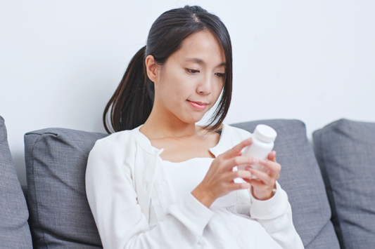a woman sitting on the couch looking at the back of a supplement bottle