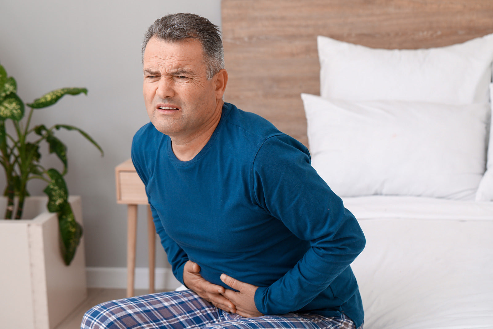 Older man sitting on bed hunched over with upset stomach